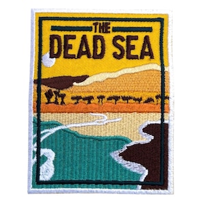 May include: Embroidered patch featuring a landscape scene with the text "THE DEAD SEA." The design includes a yellow sky, brown mountains, and a turquoise body of water. The patch is rectangular with a black border.