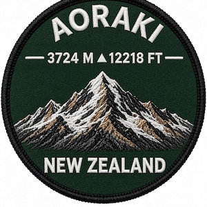 Op de afbeelding: Een ronde geborduurde patch met een donkergroene achtergrond met een besneeuwd gebergte. De tekst AORAKI staat bovenaan en NEW ZEALAND onderaan. In het midden staan 3724 M en 12218 FT met een klein driehoekig icoon.