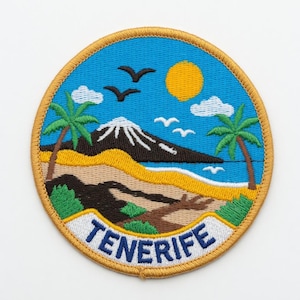 Könnte beinhalten: Gestickter Aufnäher mit einer Landschaft von Teneriffa. Das Design zeigt einen blauen Himmel mit einer gelben Sonne, weißen Wolken und fliegenden Vögeln. Ein Berg mit schneebedecktem Gipfel, Palmen und dem Wort "TENERIFE" in Weiß auf einem blauen Banner.