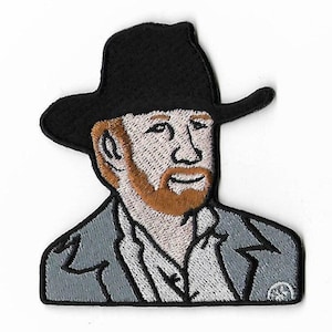 Peut inclure: Patch brodée thermocollante représentant un homme de dessin animé avec une barbe portant un chapeau de cowboy noir et une veste grise.