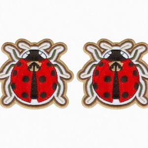 May include: Two embroidered ladybug patches. Each patch features a red body with black spots, a black head, and a tan and white decorative border. The patches are designed to be sewn onto fabric.