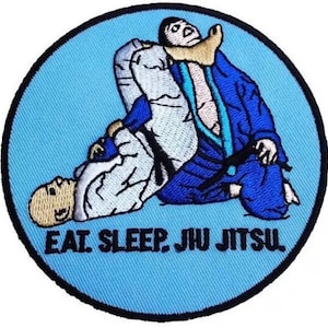 May include: A blue and white embroidered patch with two figures in a jiu-jitsu hold. The text "Eat Sleep Jiu Jitsu" is printed below the figures.