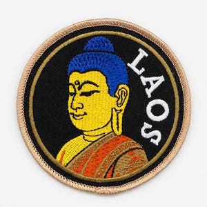 May include: Embroidered patch featuring a yellow Buddha with blue hair and an orange robe, set against a black background. The word "LAOS" is written in white. The patch has a tan border.