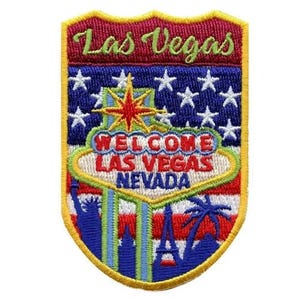 Pode incluir: Um remendo bordado com um design de bandeira americana vermelha, branca e azul. O remendo apresenta as palavras "Las Vegas" e "Welcome Las Vegas Nevada" em letras amarelas. O remendo também inclui uma imagem estilizada do letreiro de Las Vegas.