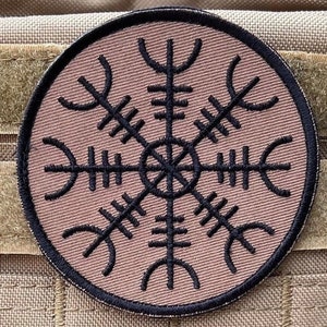 Peut inclure: Un patch en tissu brun avec un symbole Vegvisir brodé en noir, un symbole directionnel nordique, au centre.