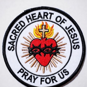 May include: A circular embroidered patch featuring a red heart encircled by a black crown of thorns, topped with a gold cross and yellow flames. The design includes gold rays and the black text SACRED HEART OF JESUS PRAY FOR US on white.