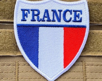 Puede incluir: Parche bordado en forma de escudo con la palabra "FRANCE" en azul sobre una franja azul. El parche muestra los colores de la bandera francesa: azul, blanco y rojo. Ideal para ropa o accesorios.