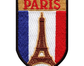 Puede incluir: Un parche bordado con forma de escudo. El escudo es negro con un borde dorado. Dentro del escudo hay un fondo blanco con los colores de la bandera francesa a los lados. La Torre Eiffel está en el centro del parche. La palabra "PARÍS" está en letras rojas en la parte superior del escudo.