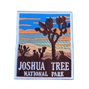 Puede incluir: Un parche bordado con el logotipo del Parque Nacional Joshua Tree. El parche representa una silueta de Joshua Tree contra un cielo de puesta de sol con las palabras "Joshua Tree National Park" en texto blanco sobre un fondo marrón.