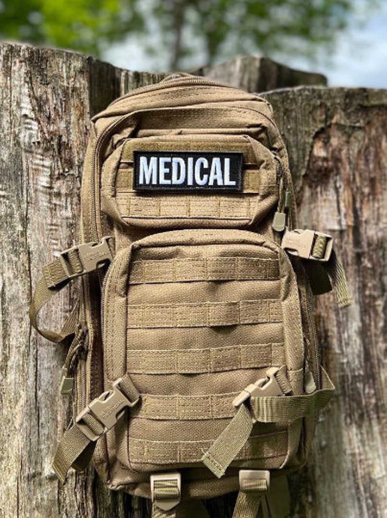 May include: A tan tactical backpack with multiple compartments and MOLLE webbing. A black and white patch with the word "MEDICAL" is centered on the front. Features adjustable straps and secure buckles for carrying medical supplies or gear.