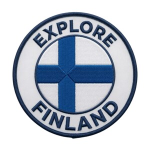 May include: A circular embroidered patch featuring a white background with a blue cross design representing the flag of Finland. The text EXPLORE is arched across the top and FINLAND is arched across the bottom in dark blue capital letters.