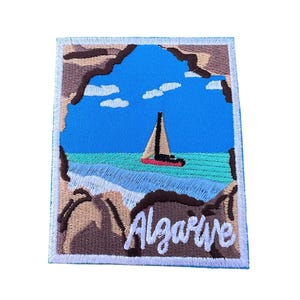 Könnte beinhalten: Gestickter Aufnäher mit blauem Himmel, weißen Wolken, einem Segelboot auf türkisfarbenem Meer und braunen Klippen. Der Text "Algarve" ist unten auf dem Aufnäher in Weiß gestickt.