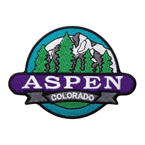 Op de afbeelding: Geborduurde patch met een berglandschap met groene bomen en een besneeuwde bergketen. De patch heeft een paarse rand met het woord "ASPEN" in wit en "COLORADO" op een grijze banner.