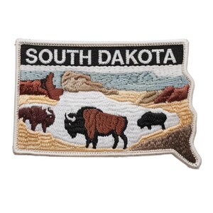 Pode incluir: Patch bordado em forma de Dakota do Sul, com o texto "SOUTH DAKOTA" em branco sobre fundo preto. O patch retrata bisontes e uma paisagem com montanhas e céu azul.