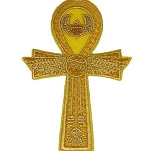 Op de afbeelding: Een gouden geborduurd Ankh-symbool met een gevleugelde scarabee bovenaan en een oog van Horus onderaan.
