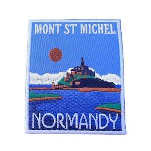 May include: An embroidered patch with a blue background featuring a white outline of the words "MONT ST MICHEL" at the top and "NORMANDY" at the bottom. The patch depicts a stylised image of the Mont Saint-Michel abbey on a small island with a red sun in the sky.