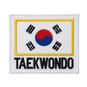 May include: A white rectangular patch featuring the South Korean flag design with a yellow border. The flag includes a red and blue yin-yang symbol and four black trigrams. The word "TAEKWONDO" is printed in black letters below the flag.