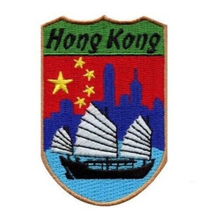 Könnte beinhalten: Ein gestickter Aufnäher in Form eines Schildes. Der Schild ist grün und braun mit den Worten "Hong Kong" in Weiß. Der Schild hat einen roten Hintergrund mit einem gelben fünfzackigen Stern und vier kleineren gelben Sternen. Der Hintergrund hat auch eine blaue Skyline mit einem weißen Dschunke im Vordergrund.