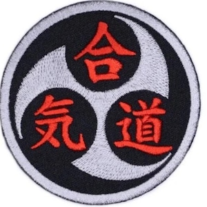 Op de afbeelding: Een ronde zwarte en witte patch met een rood geborduurd symbool. Het symbool is een triquetra met de Japanse karakters "合気道" (Aikido) erin.