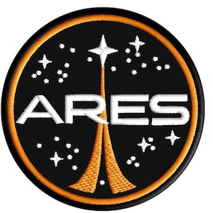 Pode incluir: Patch bordado com fundo preto, com a palavra "ARES" em letras brancas. O design inclui um lançamento de foguete estilizado em laranja e branco, rodeado por estrelas brancas e uma borda circular laranja.