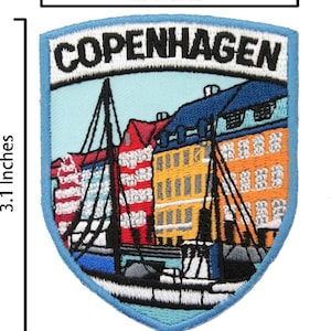 Könnte beinhalten: Gestickter Aufnäher in Schildform mit einer Darstellung von Kopenhagen, Dänemark. Der Aufnäher ist 6,35 cm breit und 7,87 cm hoch. Er zeigt farbenfrohe Gebäude in Rot, Gelb und Blau, mit dem Stadtnamen in Weiß.