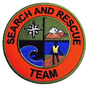 Puede incluir: Parche bordado de color naranja, verde y negro con las palabras "Search and Rescue Team" alrededor del borde. El centro del parche tiene cuatro cuadrantes con imágenes de una brújula, una montaña, una ola y una persona haciendo senderismo.