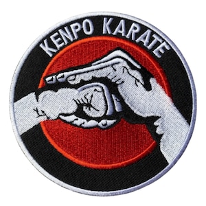 May include: Embroidered patch with the words "KENPO KARATE" in white lettering on a black background. The patch features a red circle in the center with a white hand graphic. The hand graphic is in a fist position.