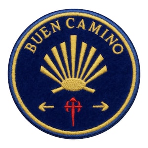 Op de afbeelding: Ronde marineblauwe patch met de gouden tekst "BUEN CAMINO". Het heeft een gouden zonnestraalontwerp, een rood kruis en pijlen. De patch is afgewerkt met een gouden rand.