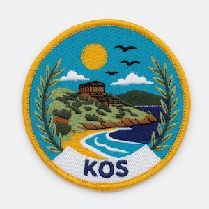 Könnte beinhalten: Runder, gestickter Aufnäher mit einer Küstenlandschaft mit Tempel, Sonne und Vögeln. Der Aufnäher hat einen blauen Hintergrund mit gelbem Rand und dem Wort "KOS" unten. Grüne Olivenzweige umrahmen die Szene.
