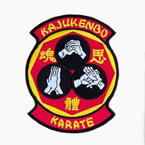 Puede incluir: Parche bordado con las palabras "KAJUKENBO" y "KARATE" en amarillo sobre fondo rojo. El parche presenta tres círculos negros con gestos de manos blancos y caracteres chinos.