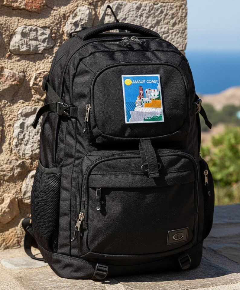 Peut inclure: Sac &agrave; dos noir avec plusieurs compartiments, fermetures &eacute;clair et sangles r&eacute;glables. Comporte un &eacute;cusson avec le texte "AMALFI COAST" et une sc&egrave;ne c&ocirc;ti&egrave;re. Comprend une poign&eacute;e sup&eacute;rieure et une poche lat&eacute;rale en filet. Id&eacute;al pour les voyages ou le quotidien.
