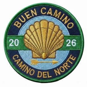 May include: Embroidered patch with a circular design. The patch features a gold scallop shell, an arrow, and the text "BUEN CAMINO CAMINO DEL NORTE" in navy blue. The numbers "20" and "26" are also present. The patch has a green border.