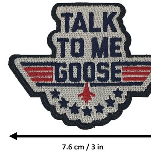 May include: A white and blue embroidered patch with a red, white, and blue wing design. The patch says "Talk to Me Goose" in navy blue lettering. The patch is 3 inches wide and 2.36 inches tall.