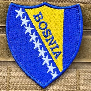 Pode incluir: Patch bordado com a bandeira da Bósnia e Herzegovina. O patch em forma de escudo tem um fundo azul com estrelas brancas na parte superior e um triângulo amarelo. A palavra "BOSNIA" é bordada em amarelo.