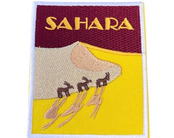 May include: An embroidered patch with a yellow background and a white border. The patch features a brown camel caravan walking up a sand dune. The word "SAHARA" is embroidered in yellow on a maroon background at the top of the patch.