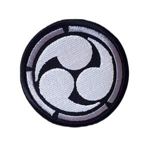 May include: A circular embroidered patch featuring a black background with a white triple comma-shaped design known as a mitsudomoe. The emblem is enclosed within a thick black border with thin white segmented lines along the outer edge.