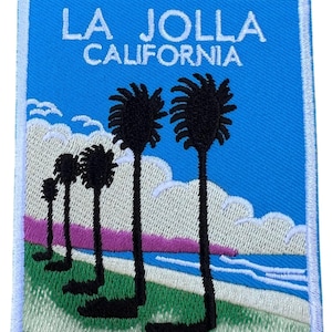 Peut inclure: Patch brodé avec un fond bleu et un texte blanc qui dit "LA JOLLA CALIFORNIE". Le patch représente une scène de plage avec des palmiers, des nuages blancs et un coucher de soleil rose.