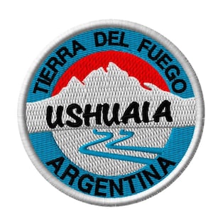 Op de afbeelding: Geborduurde ronde patch met de tekst "TIERRA DEL FUEGO" en "ARGENTINA". De patch toont een bergketen, een rivier en de stadsnaam "USHUAIA". Het ontwerp is in blauw, wit, rood en zwart, met een witte rand.