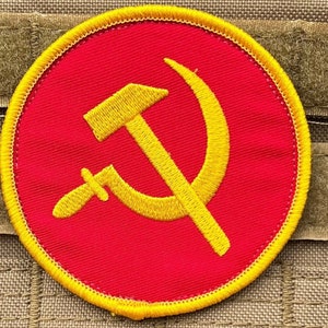 Może przedstawiać: Naszywka haftowana na czerwono z motywem młota i sierpa w kolorze żółtym. Naszywka jest okrągła i ma żółtą obwódkę.