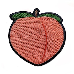 May include: An embroidered patch shaped like a peach, with a green leaf on top. The patch is peach-coloured and has a black outline.