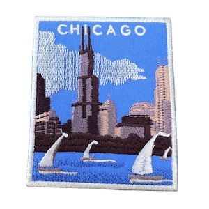 May include: Embroidered patch with a blue background featuring a cityscape of Chicago with the text "CHICAGO" at the top. The skyline includes the Willis Tower, the John Hancock Center, and other buildings. There are sailboats in the water in the foreground.
