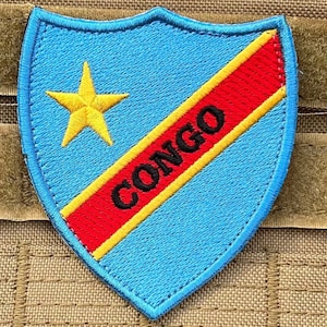 May include: A blue and yellow embroidered patch with a red diagonal stripe and the word "CONGO" in black lettering. A yellow star is in the upper left corner of the patch.