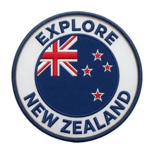 Pode incluir: Um emblema bordado circular apresentando a bandeira da Nova Zelândia no centro sobre um fundo azul escuro com estrelas vermelhas. A borda branca contém o texto azul escuro EXPLORE NEW ZEALAND escrito em uma fonte negrito sem serifa.