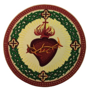 Peut inclure: Patch brodé représentant un cœur rouge avec une couronne d'épines, entouré d'une couronne de laurier verte et de quatre croix. Le cœur est en feu et a une auréole dorée.