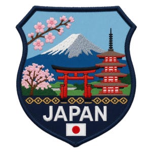 May include: A shield-shaped embroidered patch featuring a light blue sky, a snow-capped mountain, a red torii gate, a multi-tiered pagoda, and pink cherry blossoms. The word JAPAN is stitched in white letters above a small rectangular Japanese flag.