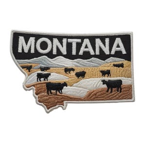 May include: Embroidered patch in the shape of Montana, featuring the state name in white block letters on a black background. The patch depicts a landscape with cows, mountains, and fields in shades of brown, tan, and white.