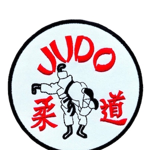 Peut inclure: Un écusson circulaire blanc avec une bordure noire. Le mot "JUDO" est écrit en lettres rouges autour du bord du cercle. Au centre du cercle se trouve une illustration en noir et blanc de deux personnes pratiquant le judo. Le mot "柔道" est écrit en lettres rouges sous l'illustration.