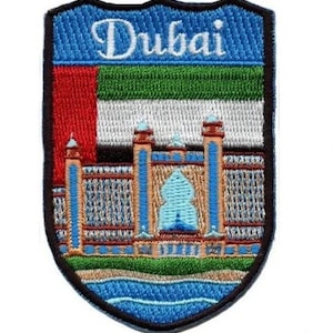 Op de afbeelding: Gestikte patch met een blauw schild met het woord "Dubai" in witte letters. Het schild toont ook de vlag van de Verenigde Arabische Emiraten en een gestileerde afbeelding van een gebouw met een blauwe koepel.