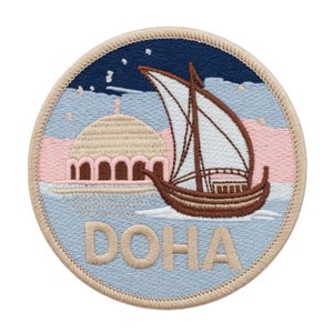May include: Embroidered patch depicting a brown dhow sailing on light blue water, with a pink and light blue sky and a mosque. The word "DOHA" is embroidered in tan. The patch has a tan border and a dark blue sky with stars.