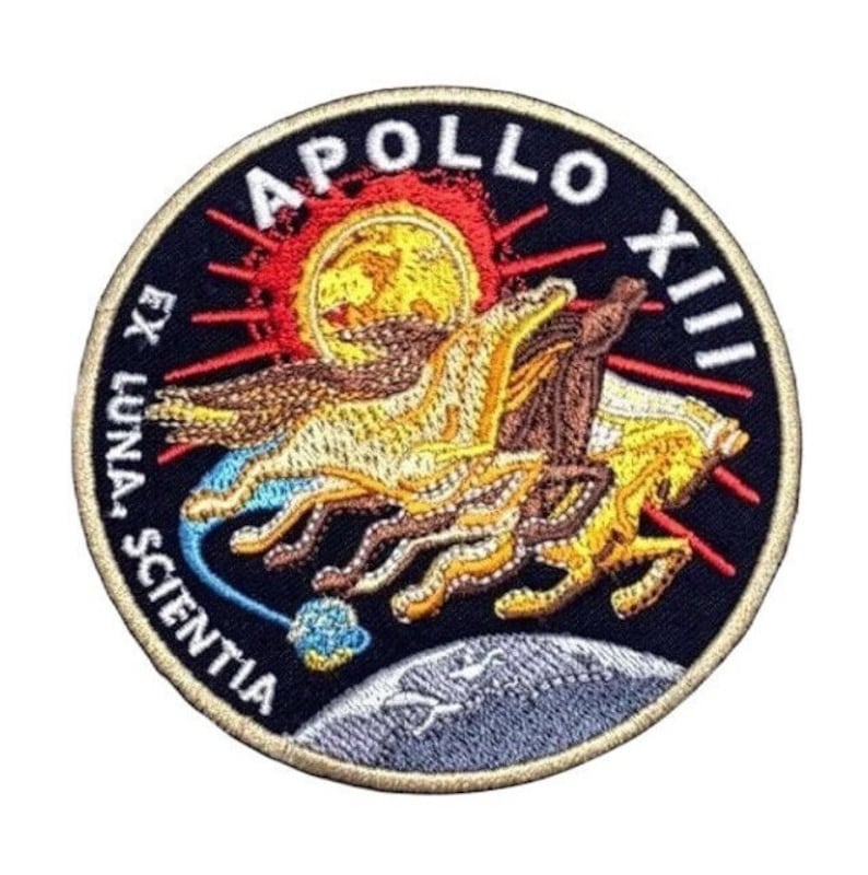 May include: A circular embroidered patch with a black background. The patch features a gold and brown image of a chariot pulled by four horses, with a red sun and rays behind it. The text "APOLLO XIII" is in a white arc above the chariot, and the text "EX LUNA SCIENTIA" is in a white arc below the chariot.